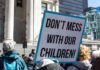 Scandal Erupts: Schools Bypass Parental Consent! Protest sign held by a crowd in an urban square