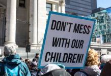 Scandal Erupts: Schools Bypass Parental Consent! Protest sign held by a crowd in an urban square