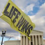 PRO-LIFE Boasts Record Fair Turnout Amid Chaos A large yellow flag with the words 'LIFE WINS' waving in front of the Supreme Court building