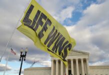 PRO-LIFE Boasts Record Fair Turnout Amid Chaos A large yellow flag with the words 'LIFE WINS' waving in front of the Supreme Court building