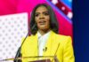 A woman in a yellow blazer speaking at a podium with a microphone