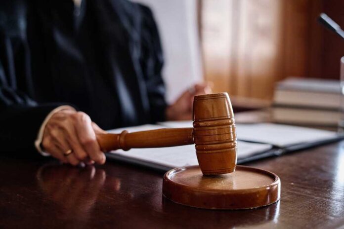 shutterstock_2378803063.jpg A judge's hand holding a gavel in a courtroom setting