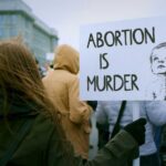 Oklahoma’s Tough Stance: Jail Time for Illegal Abortion Pills Person holding a sign that reads 'Abortion is Murder' at a protest