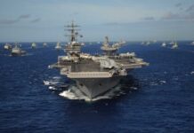 An aircraft carrier surrounded by various naval vessels in the ocean