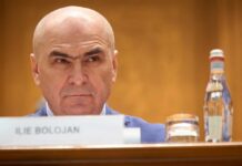 A man with a serious expression sitting at a conference table