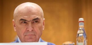 A man with a serious expression sitting at a conference table