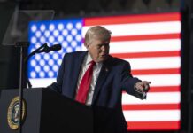 Veterans Sue Trump—VA Abortion Clash Erupts! A man in a suit gestures while speaking at a podium with an American flag in the background