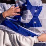 Israel Integration Plan Triggers BACKLASH People holding an Israeli flag together, showcasing unity and cultural pride