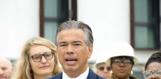 Man in a navy suit speaking at a microphone with people standing behind