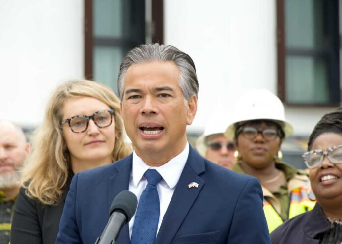 Man in a navy suit speaking at a microphone with people standing behind