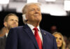 G7 Walks Tightrope on Trump Deal Smiling older man in a suit with a red tie at an indoor event
