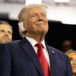 G7 Walks Tightrope on Trump Deal Smiling older man in a suit with a red tie at an indoor event
