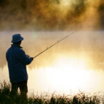 Hunting, Fishing Redefined — As Felonies A fisherman standing by a misty lake at sunrise, holding a fishing rod