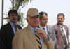 A group of men in formal attire at an outdoor event, with one man wearing a cap