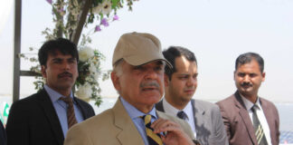 A group of men in formal attire at an outdoor event, with one man wearing a cap