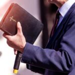 MAGA Pastor Implodes — Texts Trigger Exit A person in formal attire holding a Bible while speaking
