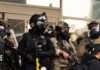 Backlash Forces ICE Training Overhaul Police officers in tactical gear wear gas masks during a crowd control operation