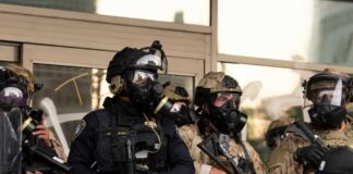 Police officers in tactical gear wear gas masks during a crowd control operation