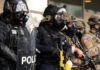 DHS Zero Tolerance Sparks First Amendment Clash Police officers in tactical gear and gas masks standing in formation