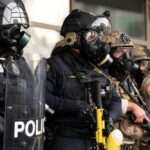 Police officers in tactical gear and gas masks standing in formation