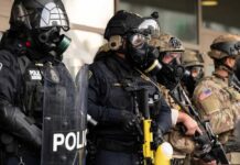DHS Zero Tolerance Sparks First Amendment Clash Police officers in tactical gear and gas masks standing in formation