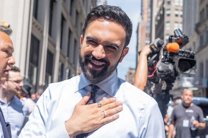 Zohran,Mamdani,Who,Is,Likely,To,Become,Next,Mayor,Of A smiling man in a light blue shirt gestures with his hand in an outdoor urban setting