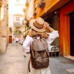 Traveler with hat and backpack facing a grand fountain and arch