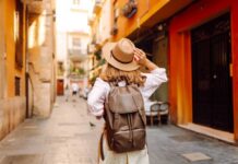 Traveler with hat and backpack facing a grand fountain and arch