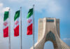 Shadow Rulers Exposed — Deals Won’t Save Iran Three Iranian flags in front of the Azadi Tower against a blue sky