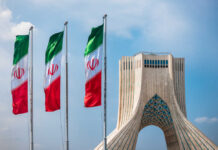 Shadow Rulers Exposed — Deals Won’t Save Iran Three Iranian flags in front of the Azadi Tower against a blue sky