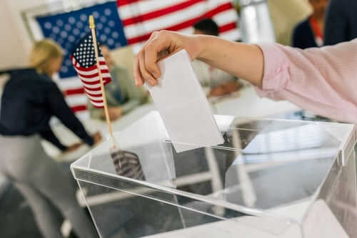 us-ballot2463011893jpg Hand placing ballot in box with American flag nearby