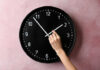 Hand adjusting a wall clock on pink background