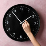 Hand adjusting a wall clock on pink background