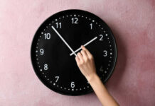 Hand adjusting a wall clock on pink background