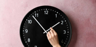 Hand adjusting a wall clock on pink background