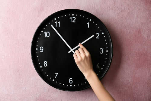 clock1078581419 Hand adjusting a wall clock on pink background