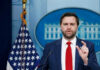 Tariff Shock: Vance Ditches Free-Market Playbook Man speaking at podium with US flag behind