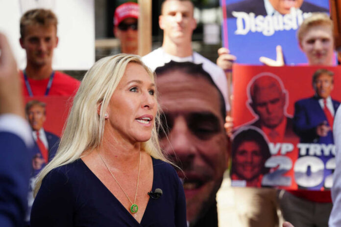 marjorie-taylor-greene-gave-interviews2351699623jpg Woman speaking at outdoor event with protest signs in background