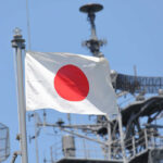 Silhouettes of soldiers saluting the Japanese flag against a sunset