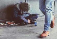 Harm Reduction or Public-Funded Paraphernalia? Person sitting on sidewalk with hood up beside a paper cup