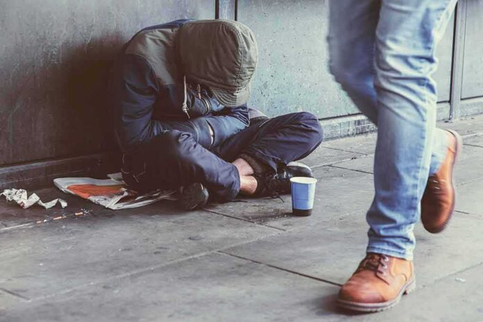 Person sitting on sidewalk with hood up beside a paper cup