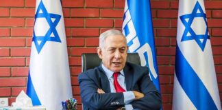 man in suit seated at desk with Israeli flags