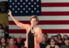 Warren’s IRS Beast: Billionaires Cornered A woman speaking into a microphone with an American flag backdrop