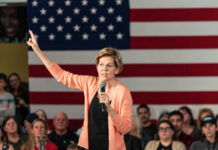 Warren’s IRS Beast: Billionaires Cornered A woman speaking into a microphone with an American flag backdrop