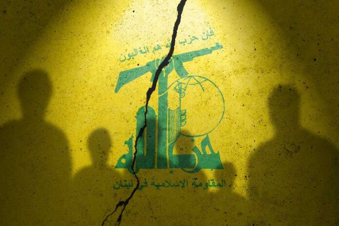 Flag,Of,Terrorist,Organization,Hezbollah,Painted,On,The,Concrete,Wall Silhouettes of individuals against a yellow wall featuring Hezbollah's emblem
