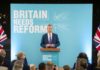 Probe Paused—Farage Gambles Everything A politician delivering a speech at a podium with British flags in the background