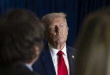 Iran Hit List: Trump Targeted? A serious-looking man in a suit with a red tie, surrounded by blurred figures