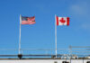 Tariffs Trigger Canadian Travel Meltdown American and Canadian flags flying on poles against a clear blue sky