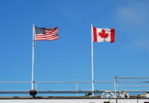 Tariffs Trigger Canadian Travel Meltdown American and Canadian flags flying on poles against a clear blue sky