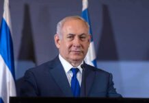 Netanyahu Showdown Brewing In New York man in suit at podium with flags in background